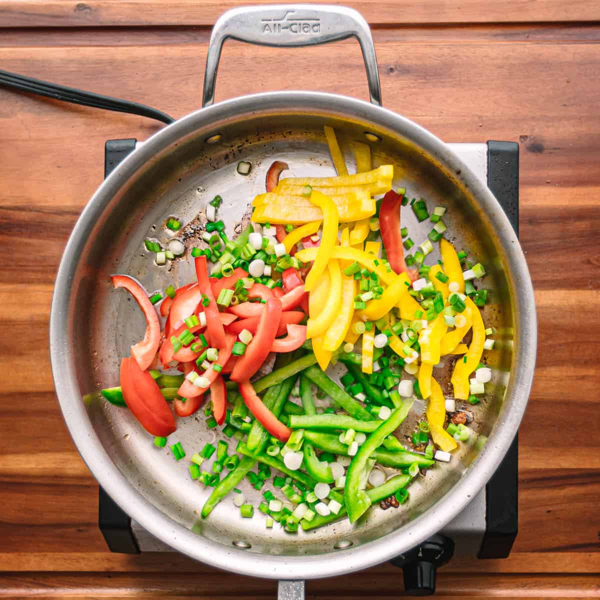 Cook the red, green, and yellow bell peppers along with the green onions for about 3 minutes, or until they become tender on medium heat.