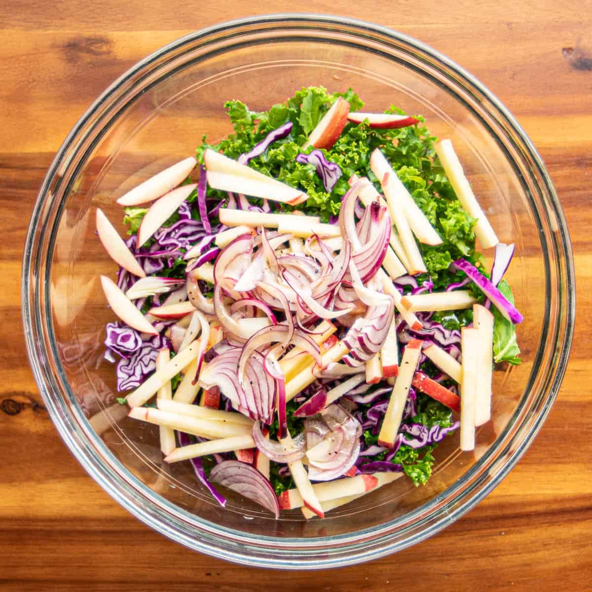 In a large mixing bowl, combine the shredded kale, red cabbage, and apple matchsticks.