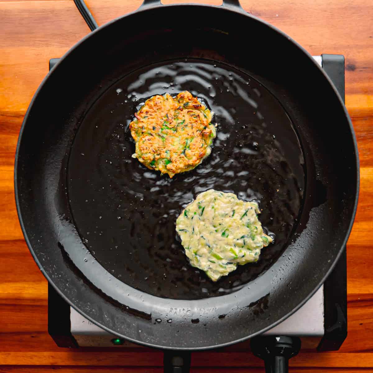 Once the oil is hot and ready, use a spoon to scoop portions of the zucchini mixture and gently place them into the heated oil. Slightly flatten each portion with the back of the spoon to shape them into fritters.