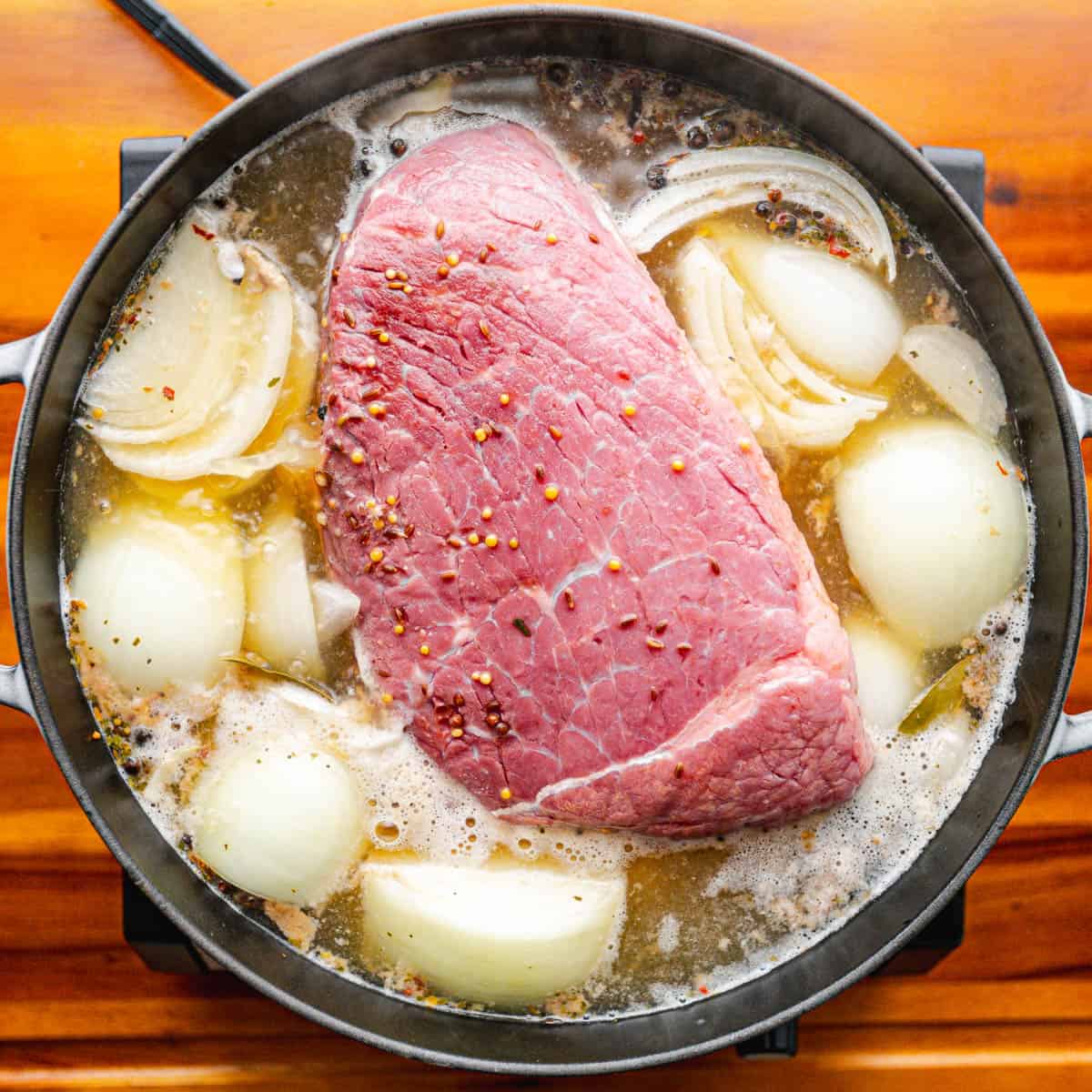 Place the uncooked corned beef, along with the seasoning packet, garlic, onion, bay leaves, and broth, into the Dutch Oven.