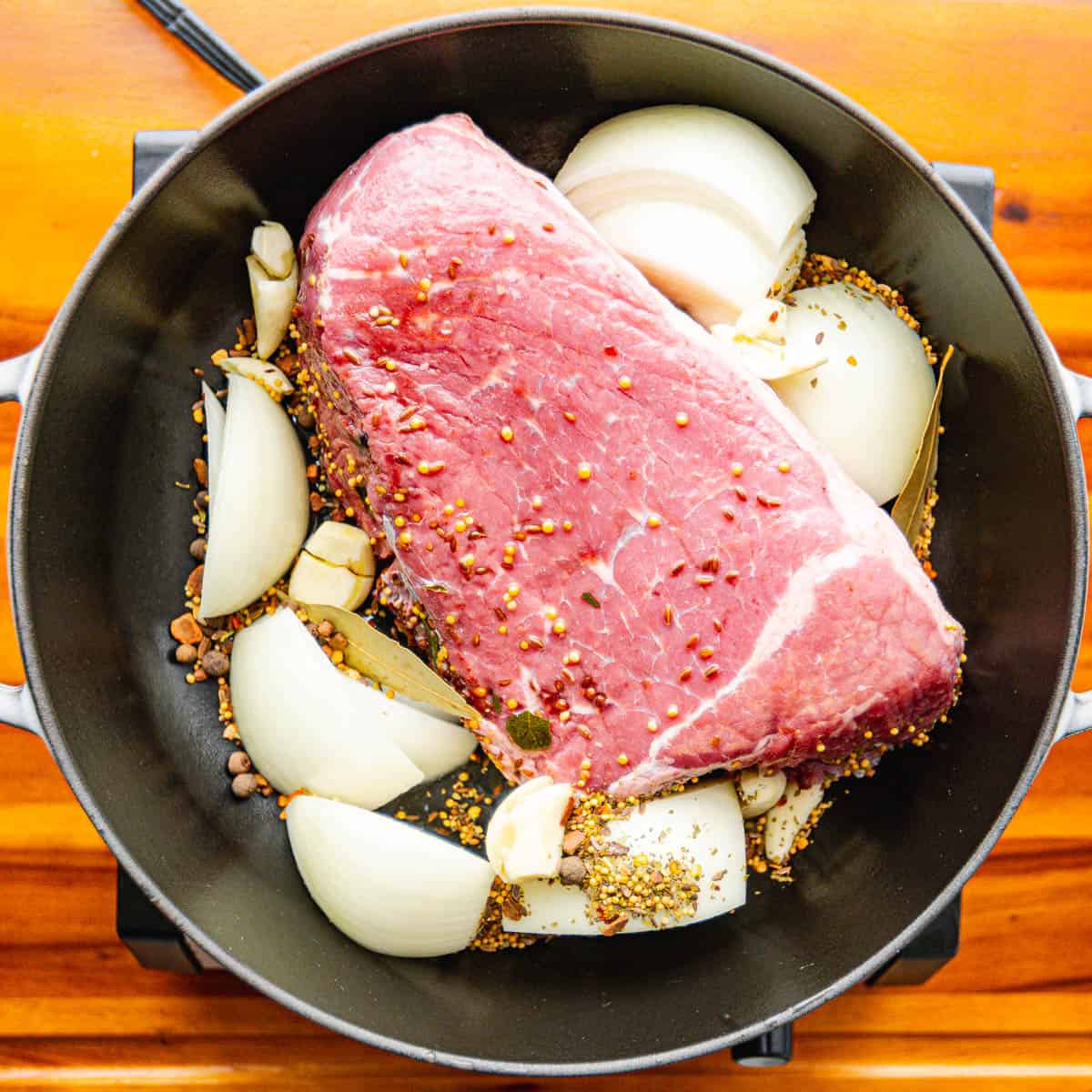 Place the uncooked corned beef, along with the seasoning packet, garlic, onion, bay leaves, and broth, into the Dutch Oven.