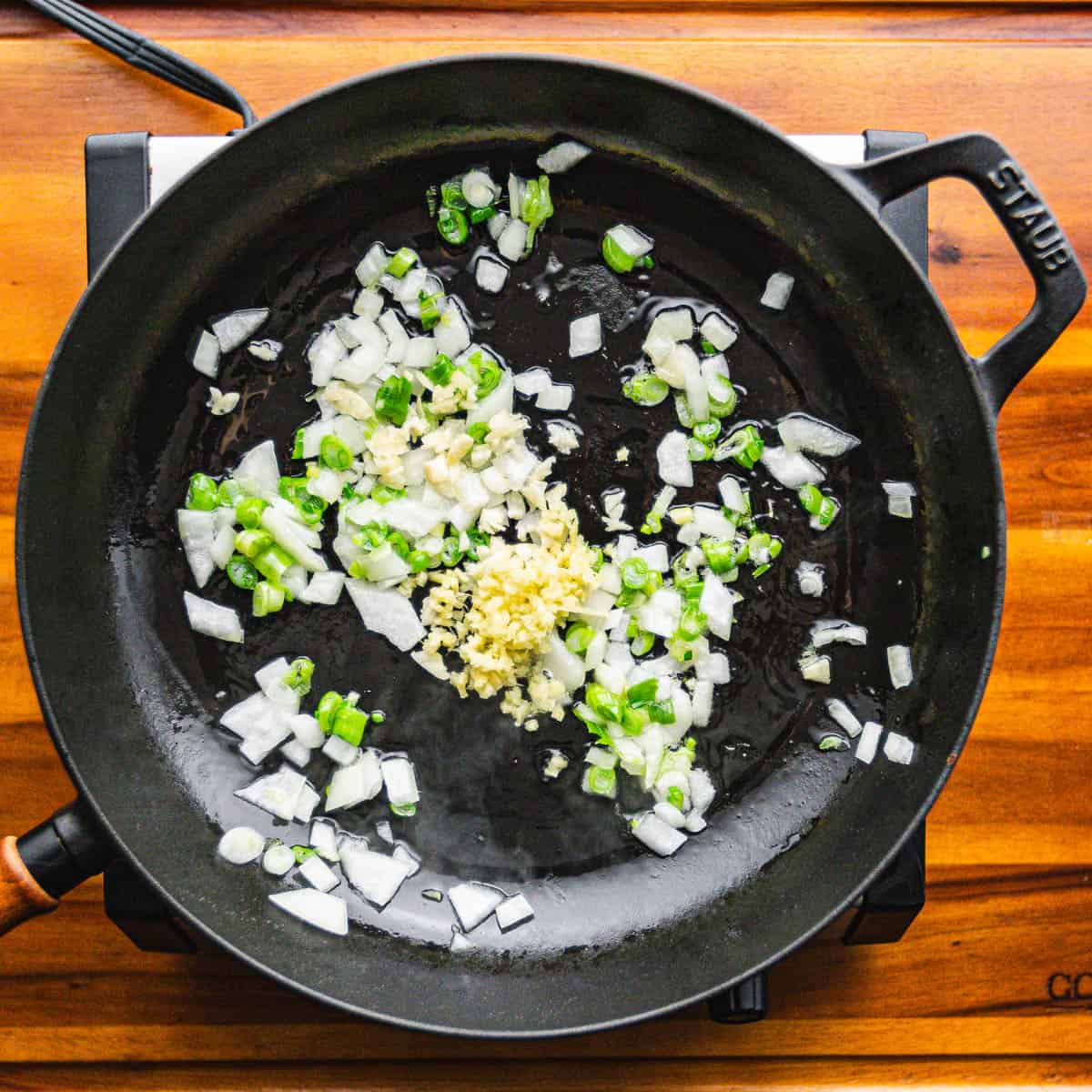  In a large wok or heavy bottomed skillet, heat oil over medium-high heat. Cook the onion and green onion (white and light green parts only) for 1 minute. Add garlic and ginger, cook for another minute.