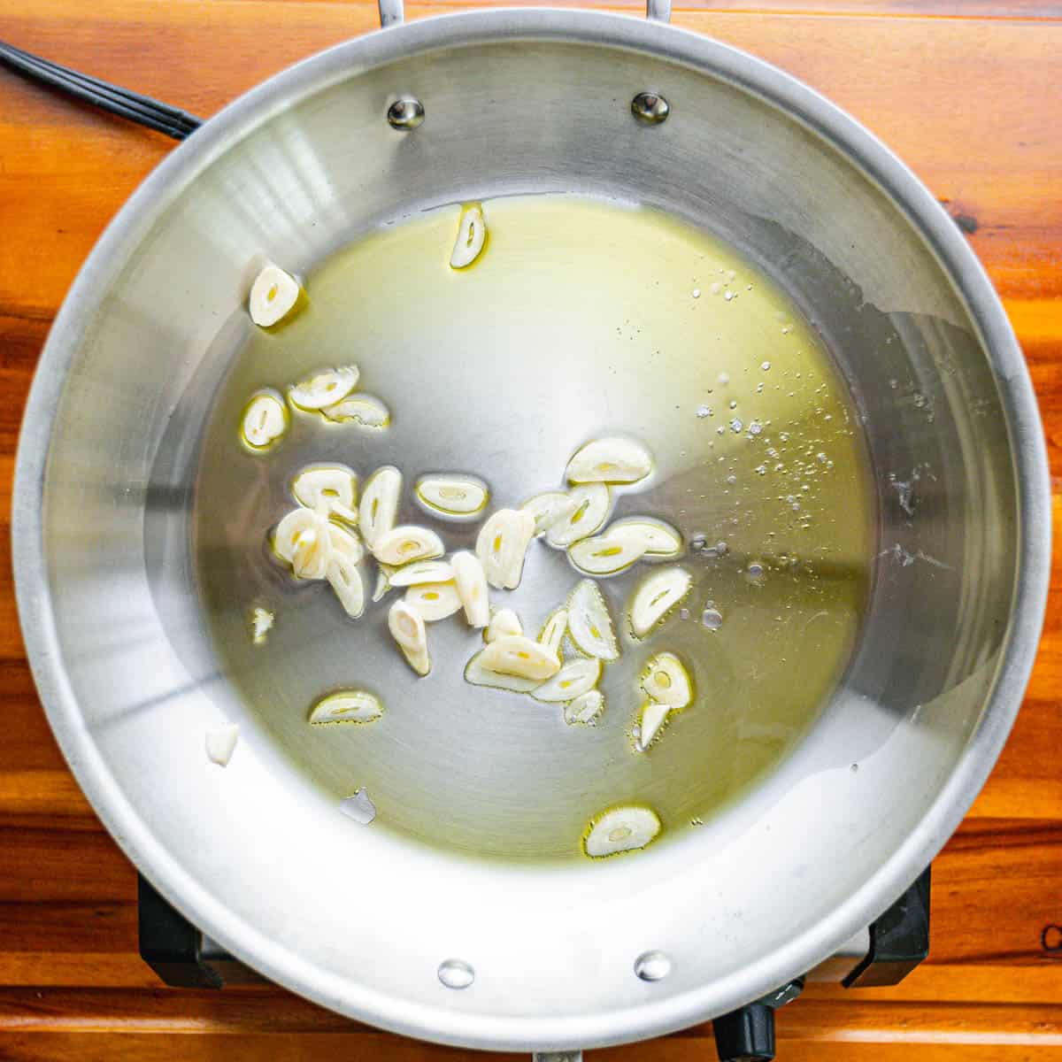 Once the oil is hot, add sliced garlic to the pan. Sauté the garlic for about a minute until it becomes fragrant, being careful not to let it burn.