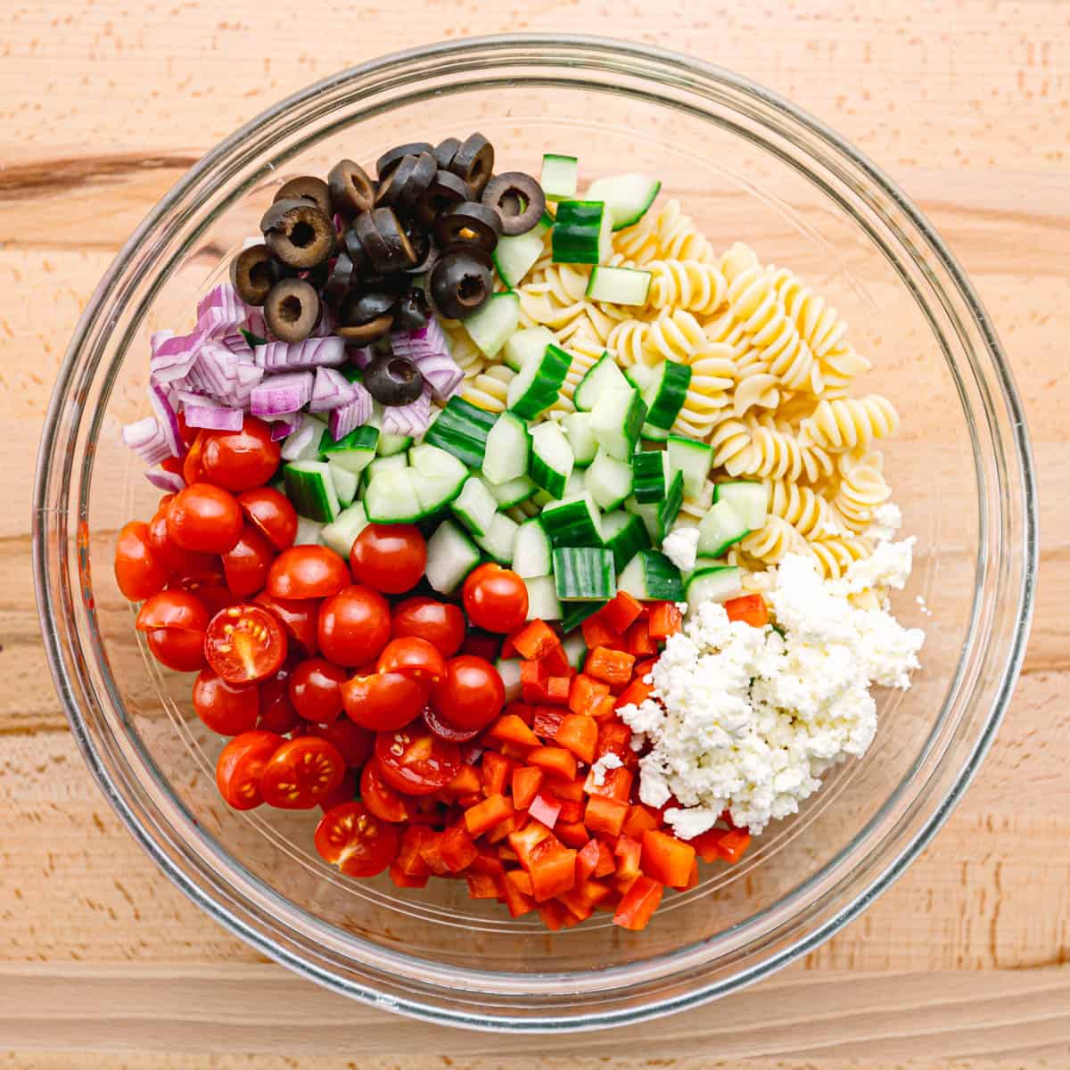 In a large mixing bowl, toss together the cooled pasta, cherry tomatoes, cucumber, red onion, Kalamata olives, and feta cheese. Pour the dressing over the salad and gently toss until everything is evenly coated.