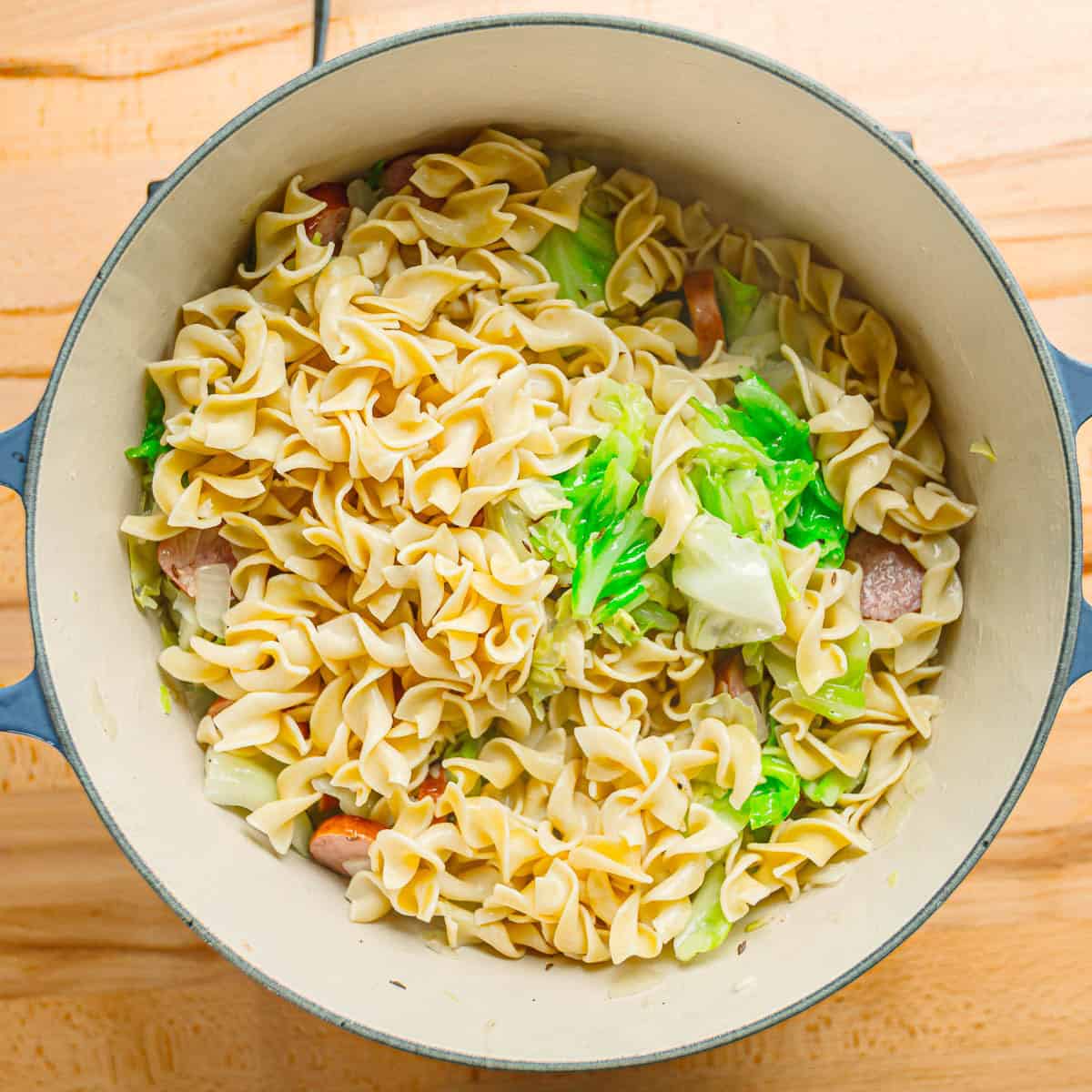 Adding egg noodles to cabbage. 