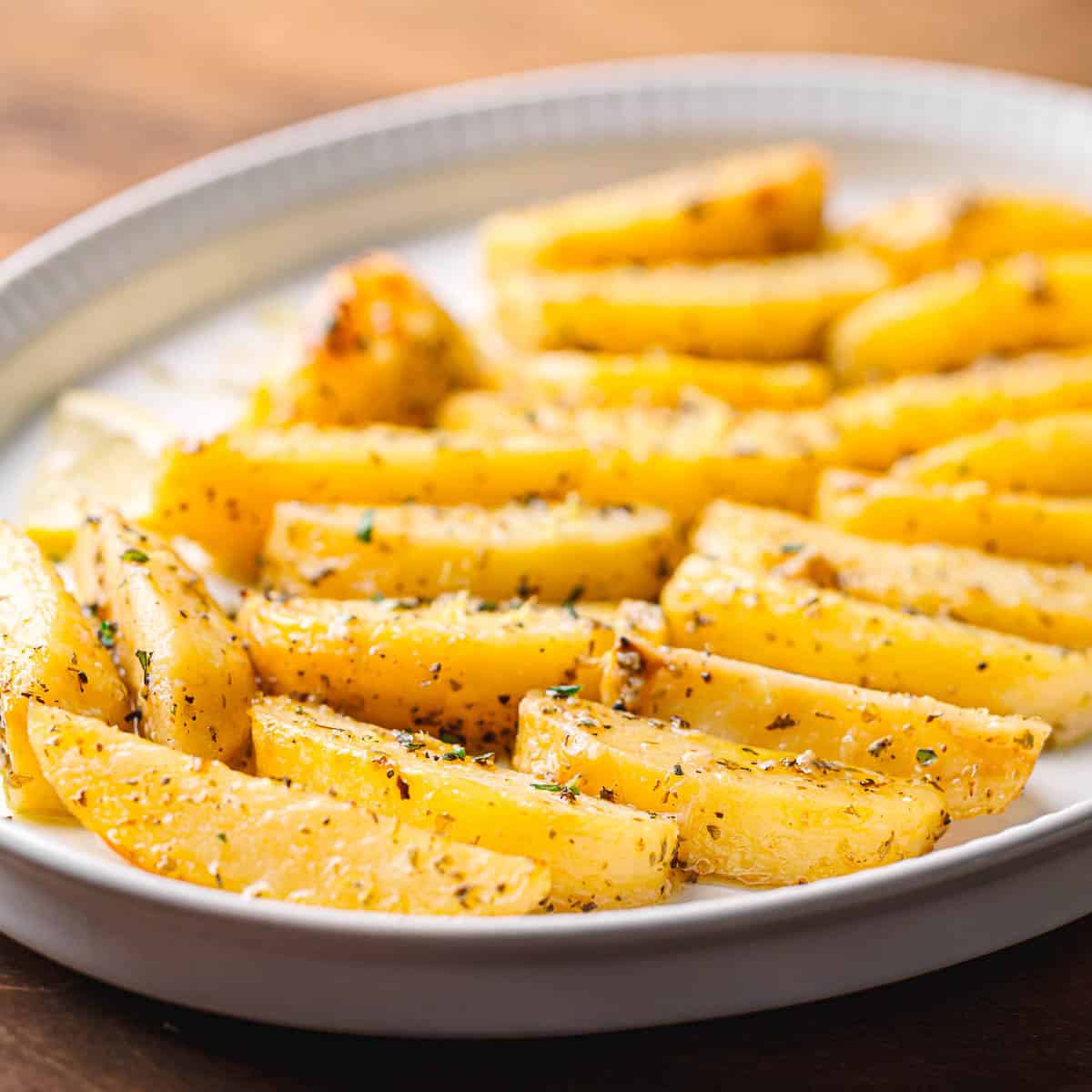 Golden Greek Lemon Potatoes served in a white oval bowl, drizzled with olive oil and sprinkled with oregano.