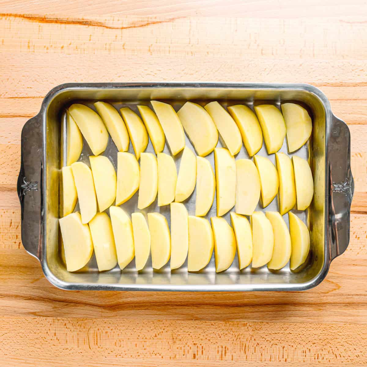 Greek Lemon Potato wedges arranged in a single layer in a large baking pan, ready for roasting.
