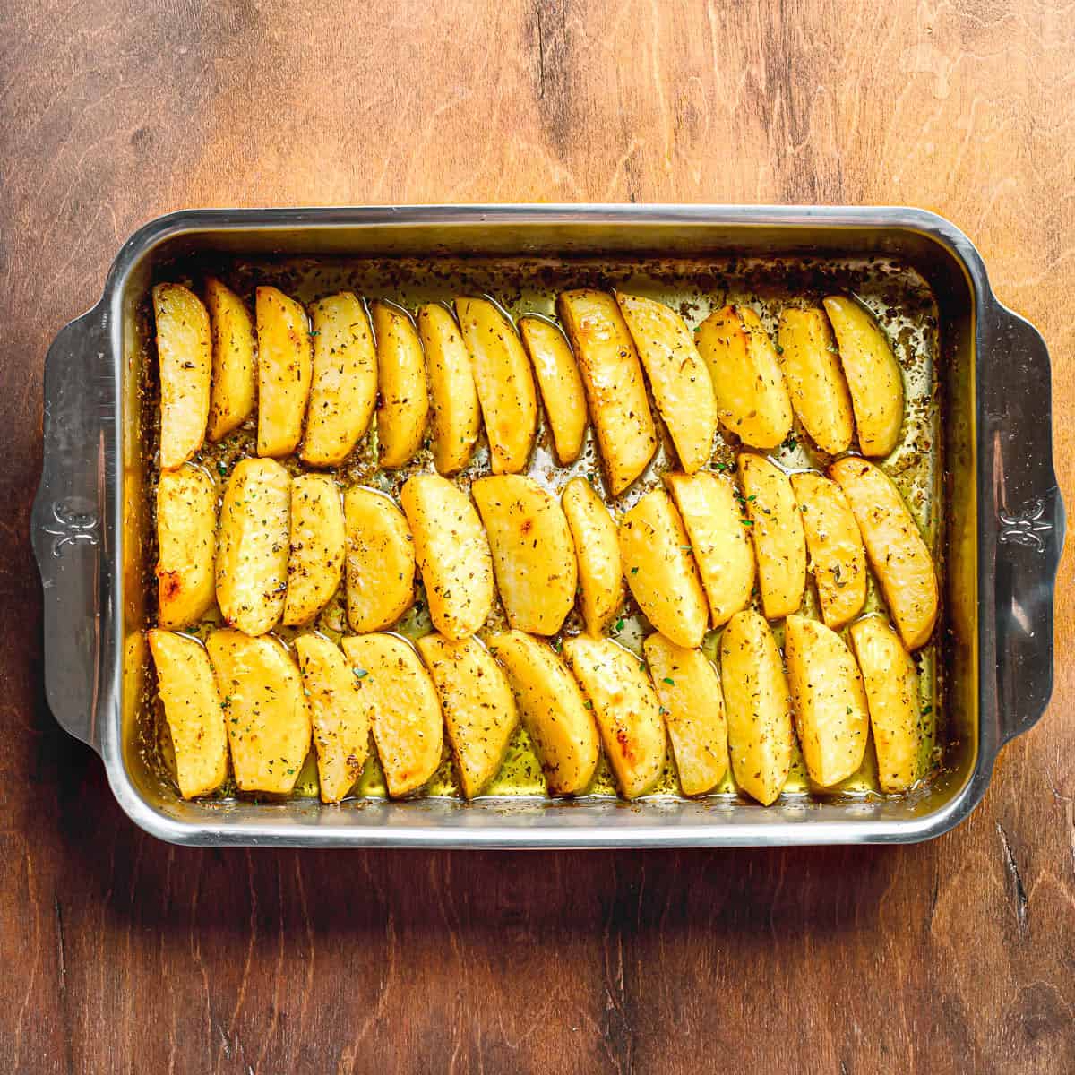 Seasoned Greek Lemon Potato wedges spread evenly in a baking pan.