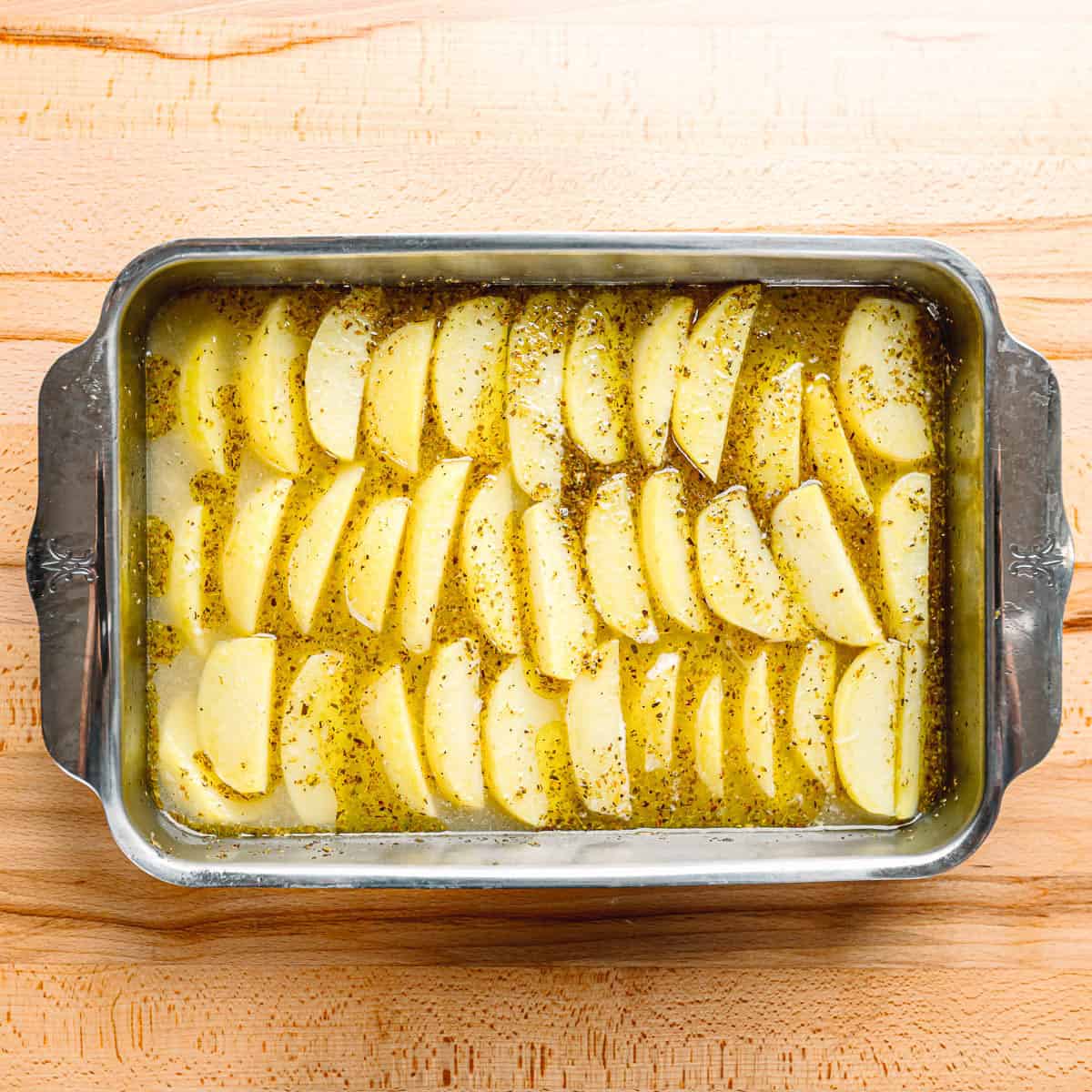 Greek Lemon Potato wedges arranged in a single layer in a large baking pan, ready for roasting.
