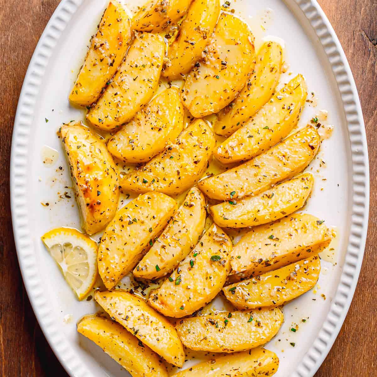 Golden Greek Lemon Potatoes served in a white oval bowl, drizzled with olive oil and sprinkled with oregano.