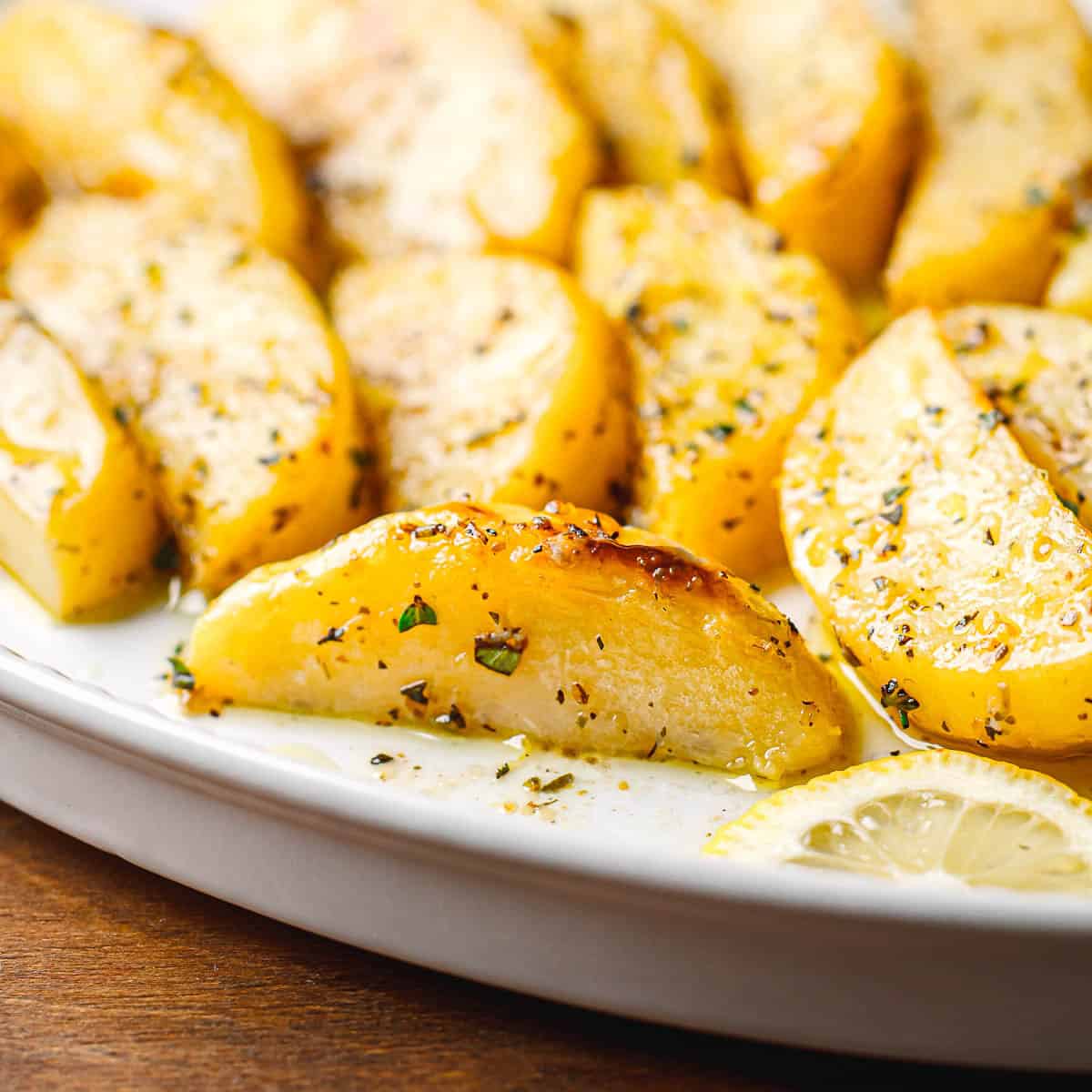 Golden-brown Greek Lemon Potatoes garnished with lemon zest, lemon wedges, and freshly chopped oregano. 