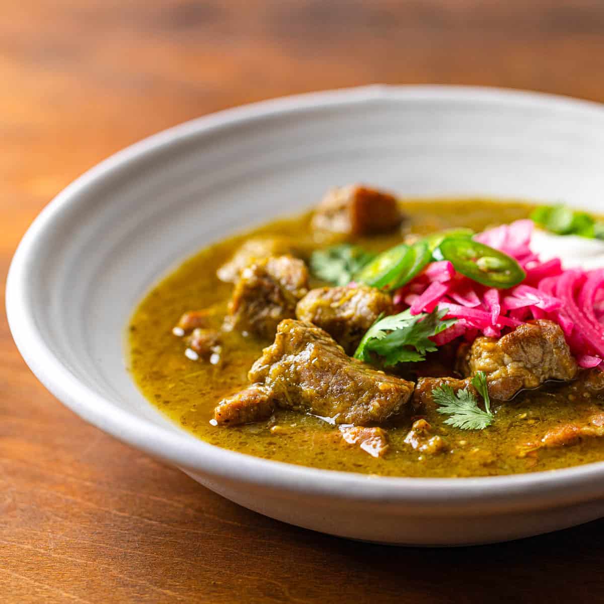 Pork chili verde with sour cream, cilantro, and pickled onion in a white bowl. 