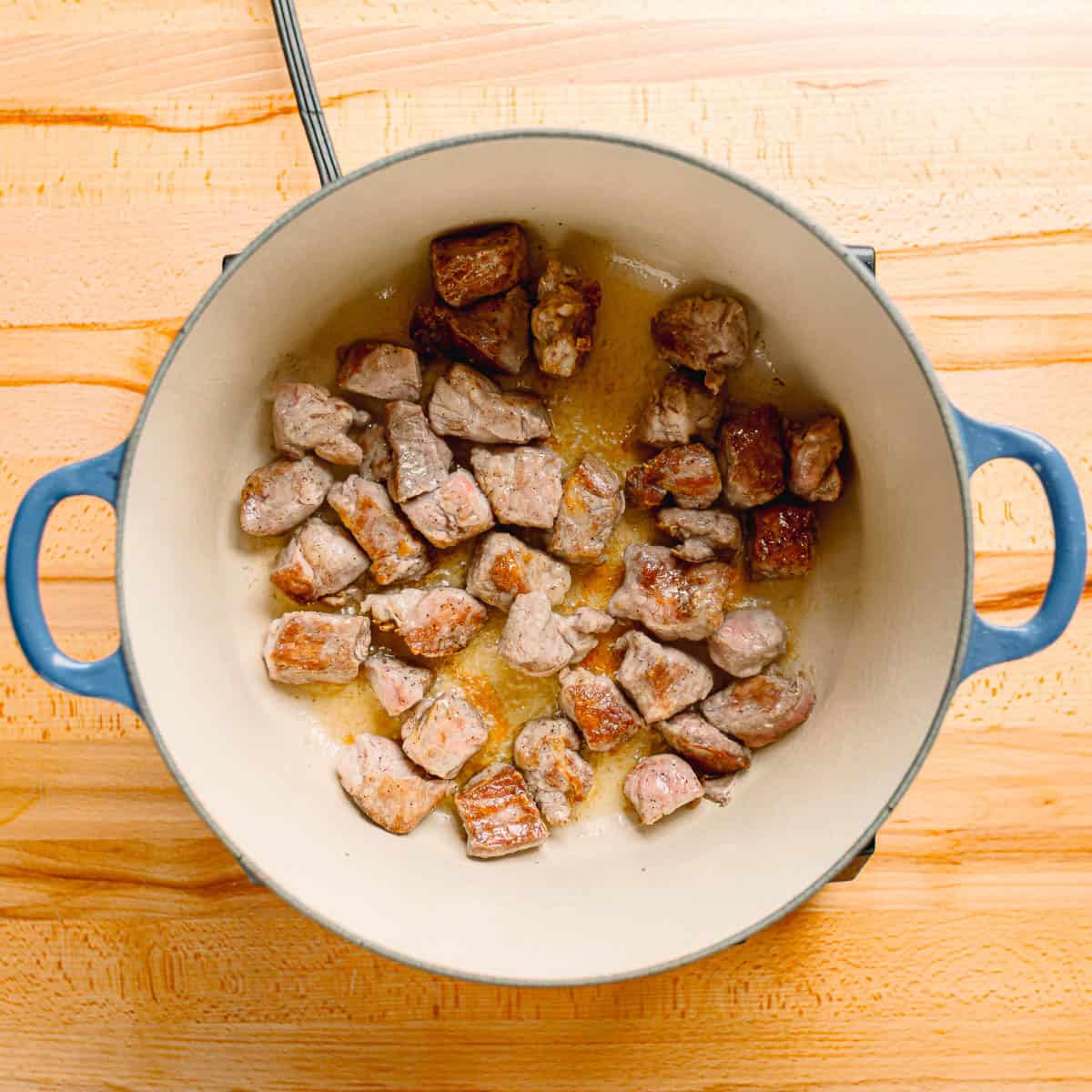 Pork browning in a large Le Creuset Dutch oven. 
