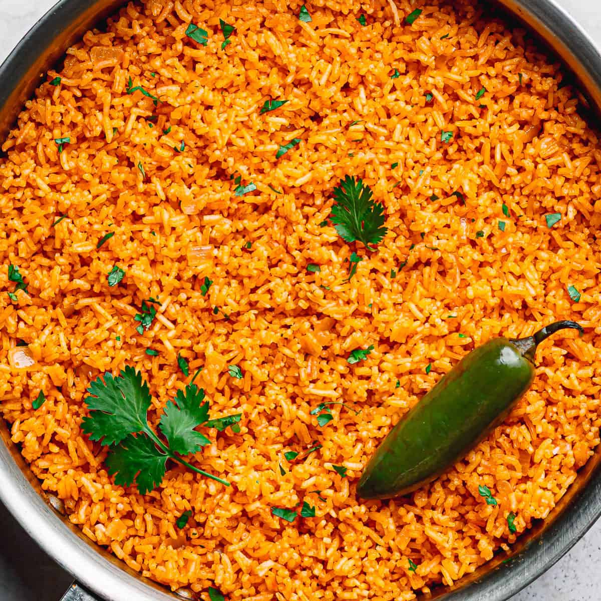 Fluffy Mexican rice in a large sauté pan garnished with fresh cilantro and jalapeño.