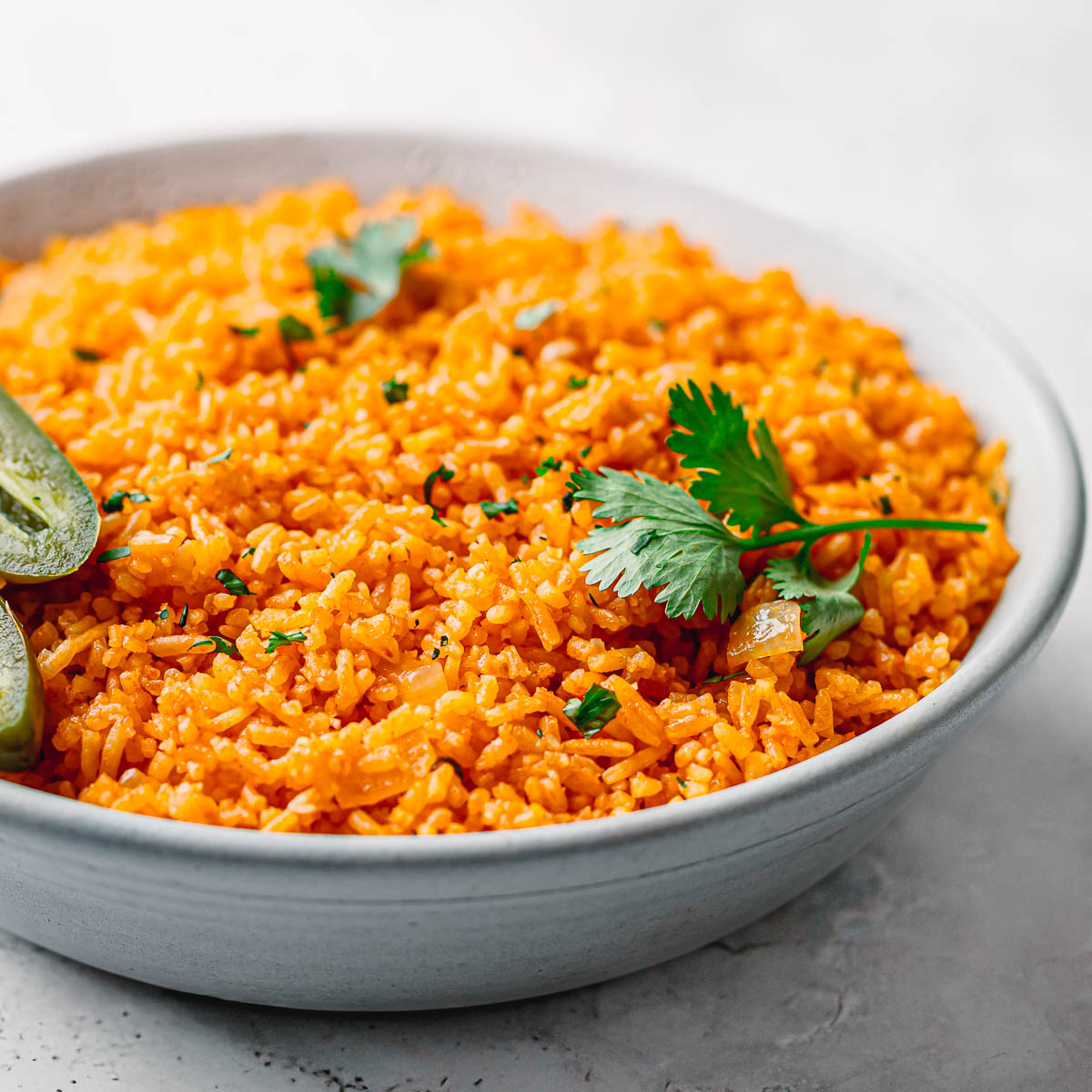 Mexican rice in a bowl garnished with fresh cilantro and sliced jalapeños.