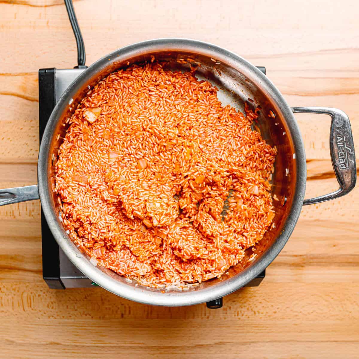 Mixing tomato sauce, cumin, and salt into sautéed rice and onions.