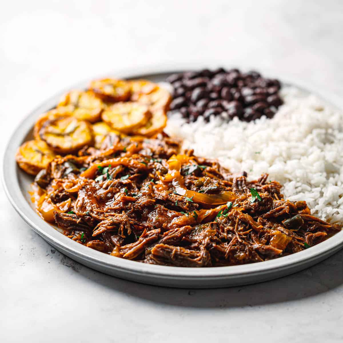 Cuban ropa vieja meal with rice, black beans, and crispy plantains.