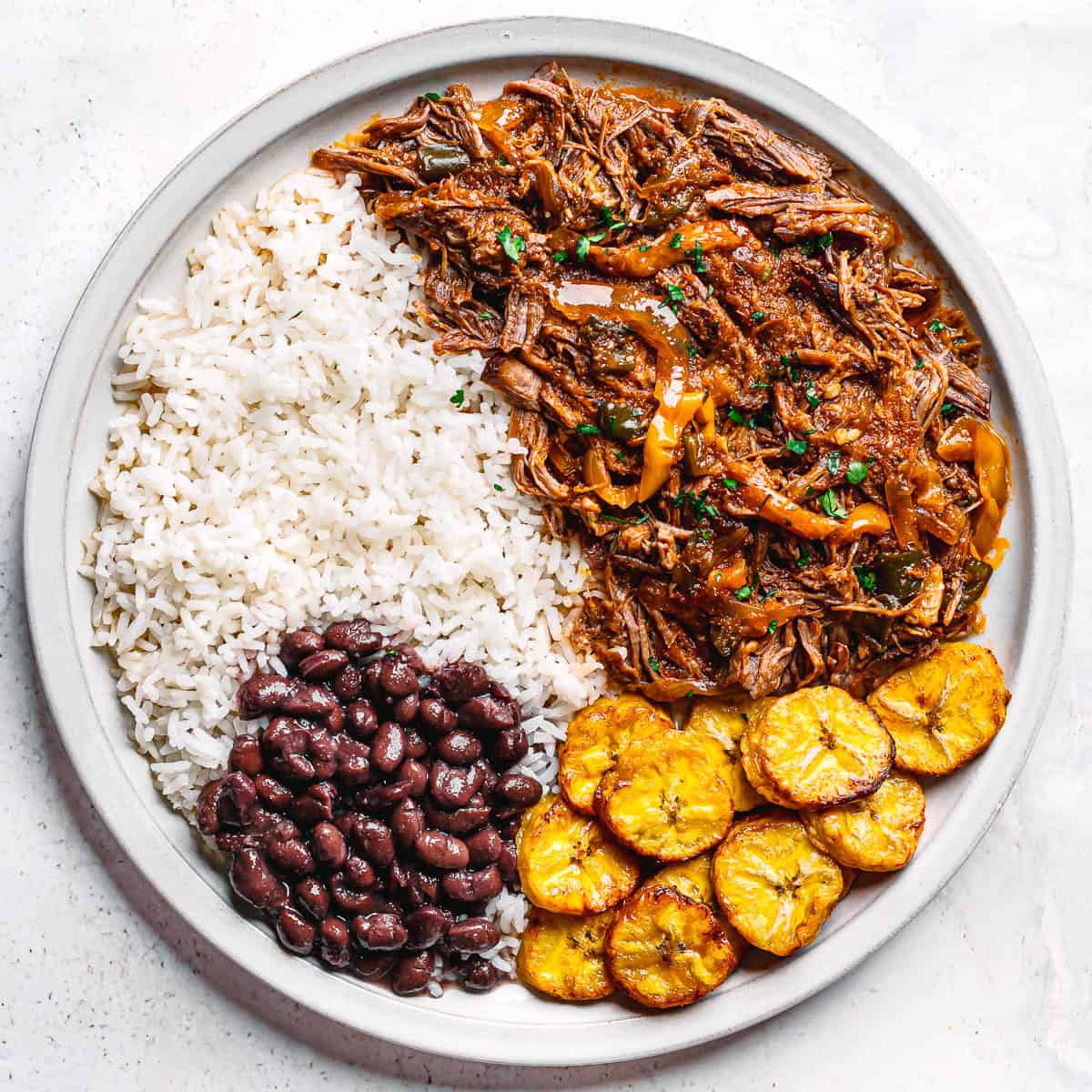 Plate of Cuban ropa vieja with white rice, black beans, and crispy air-fried plantains.