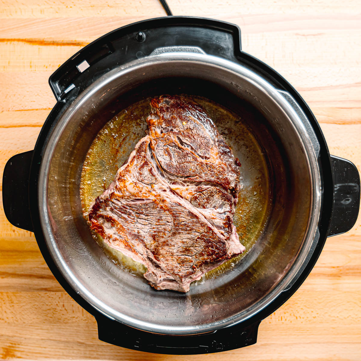 Browned chuck roast pieces sizzling in a pot with olive oil.