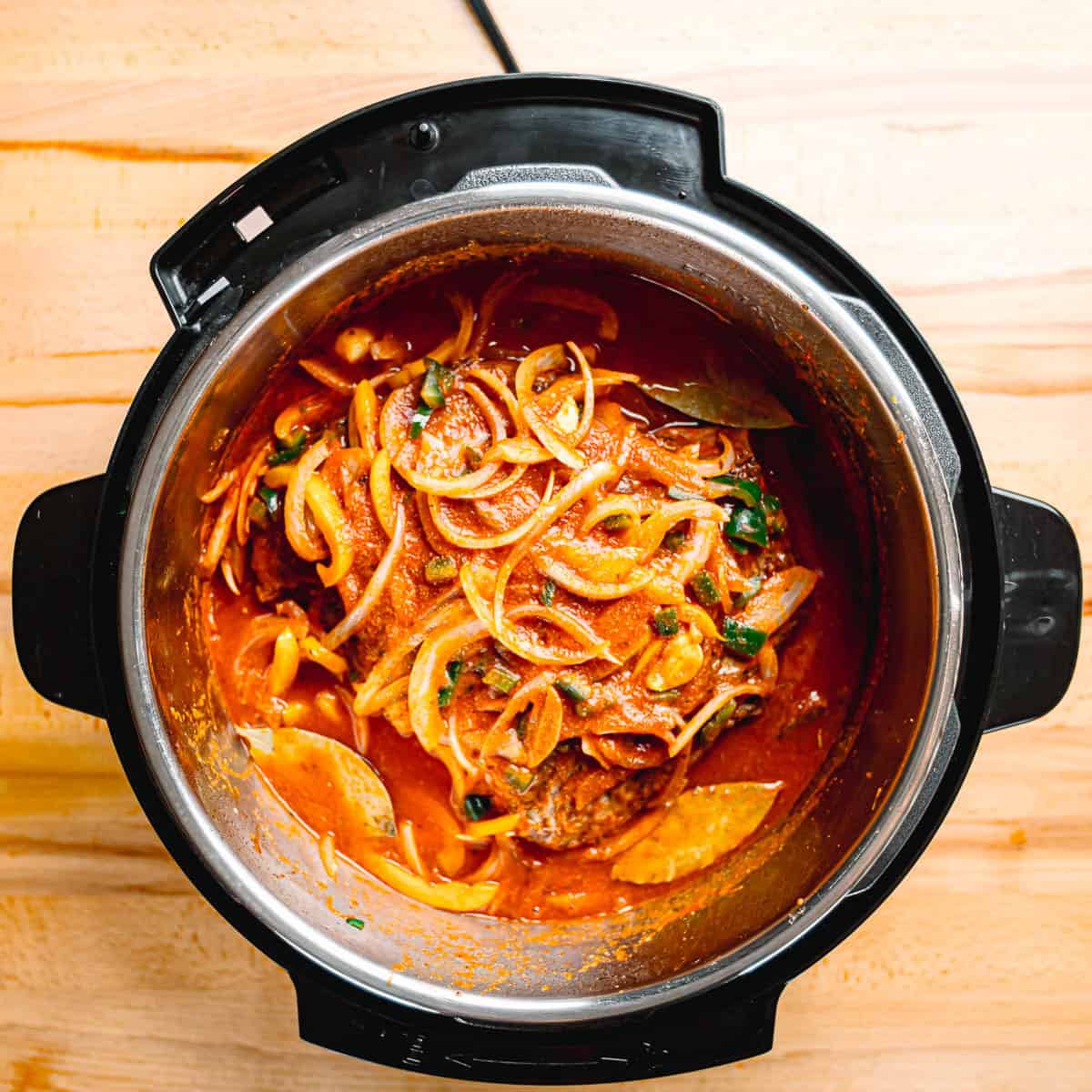 Browned beef pieces covered in tomato and pepper sauce inside an Instant Pot.