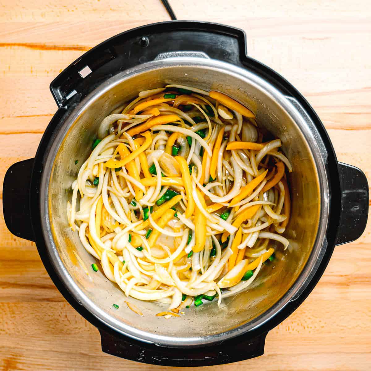 Sliced onions, red bell pepper, and poblano pepper cooking in a pot.