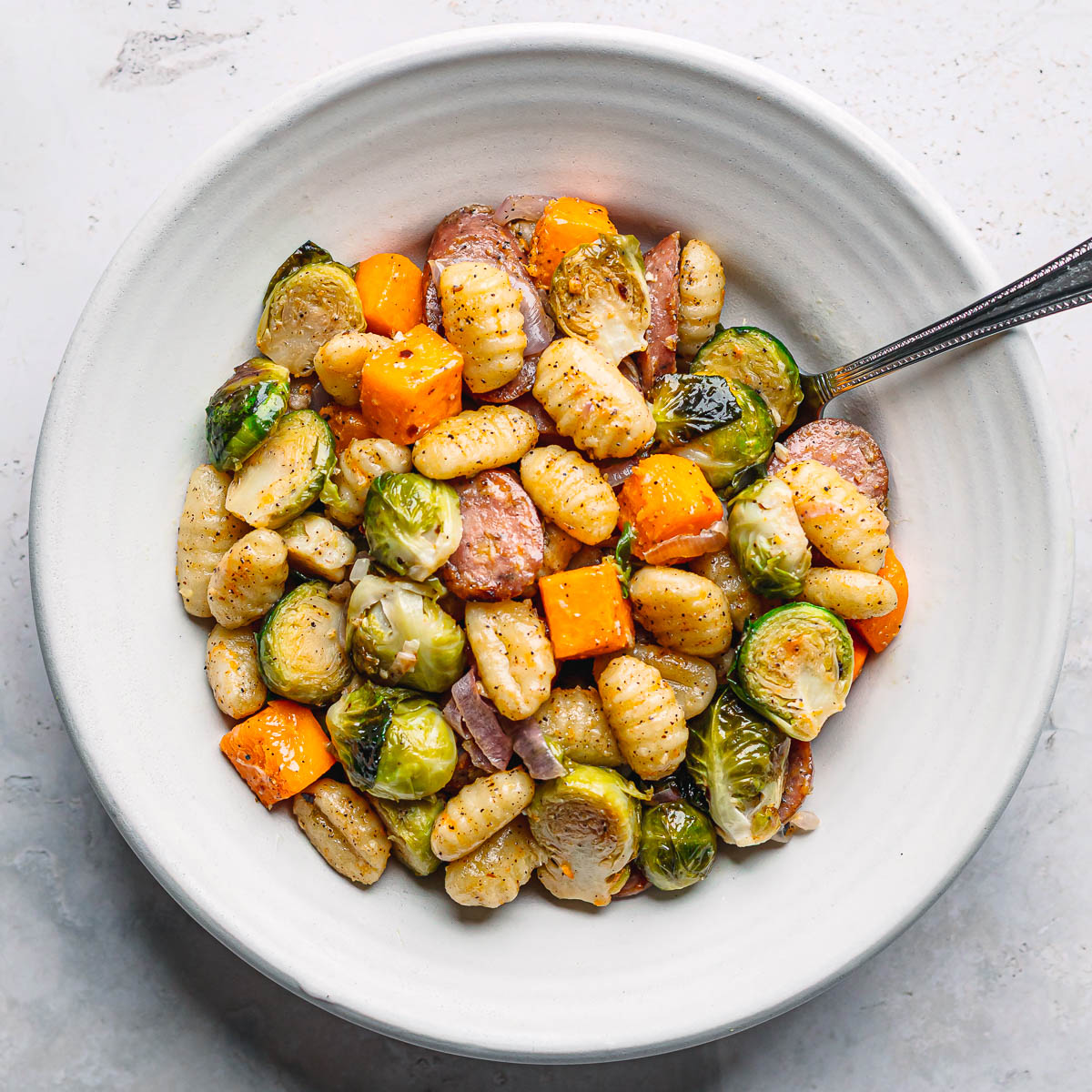 Roasted chicken sausage, Brussels sprouts, and butternut squash served in a white bowl.