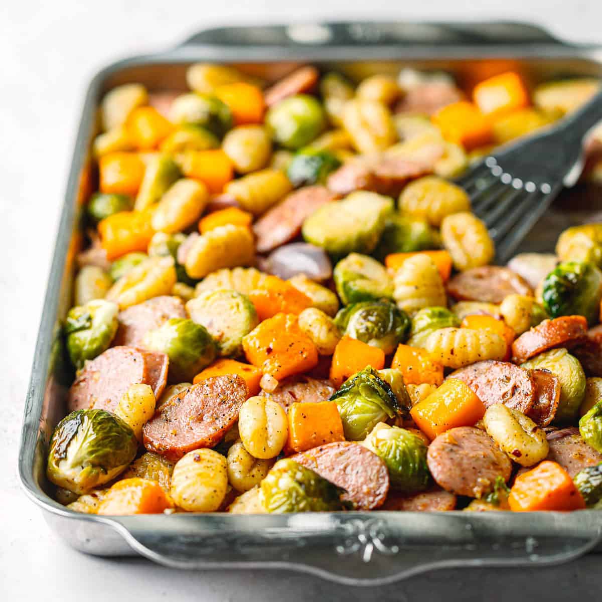 Full sheet pan meal of chicken sausage, Brussels sprouts, butternut squash, and gnocchi ready to serve.