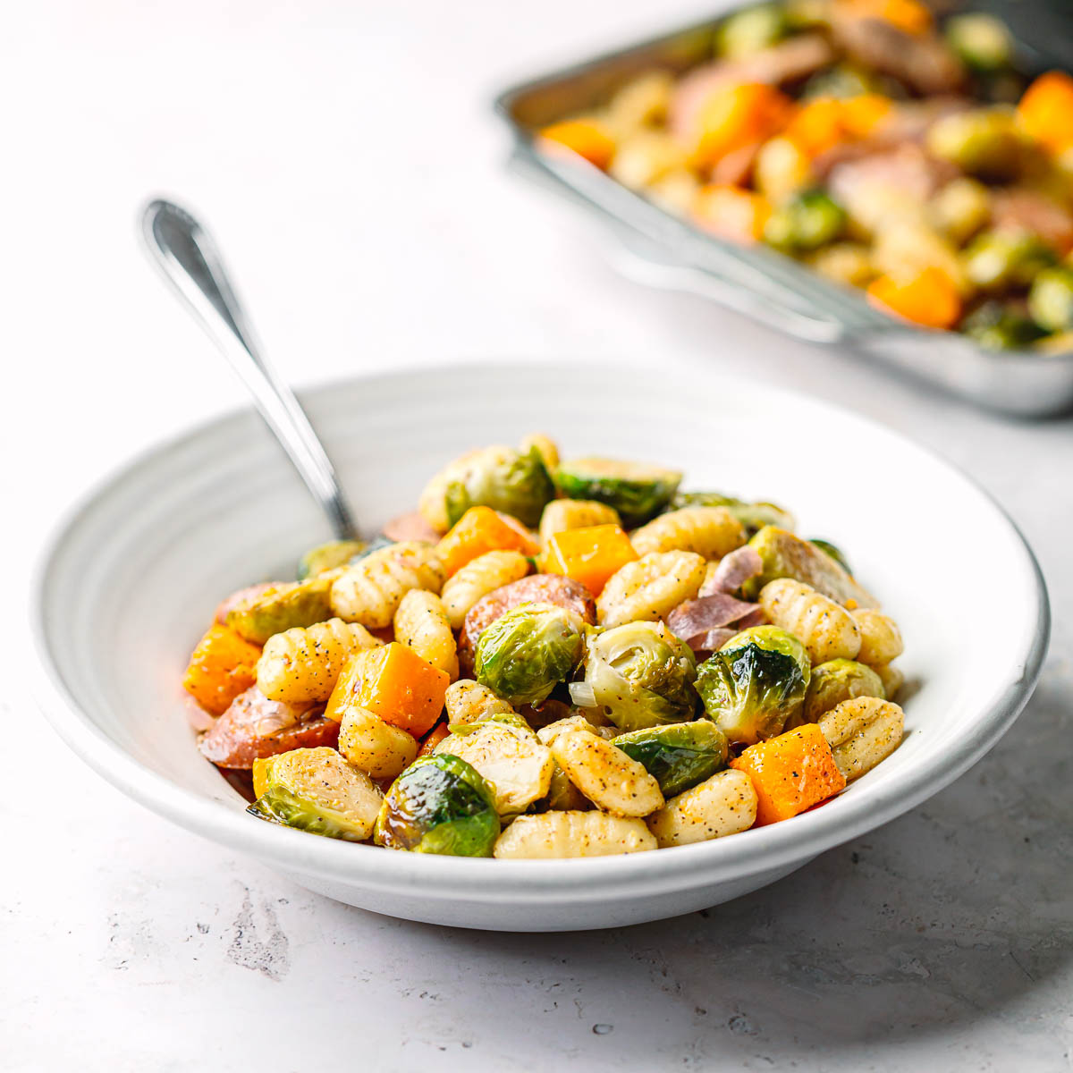 Bowl of sheet pan chicken sausage with Brussels sprouts, butternut squash, gnocchi, and shallots, drizzled with lemon mustard honey sauce.