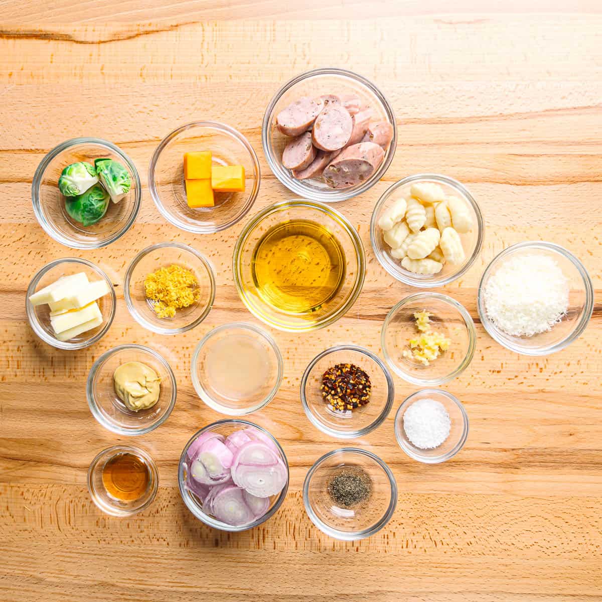 All ingredients for sheet pan chicken sausage with Brussels sprouts and butternut squash on a table, including chicken sausage, Brussels sprouts, butternut squash, gnocchi, shallots, garlic, olive oil, butter, lemon, mustard, and honey.