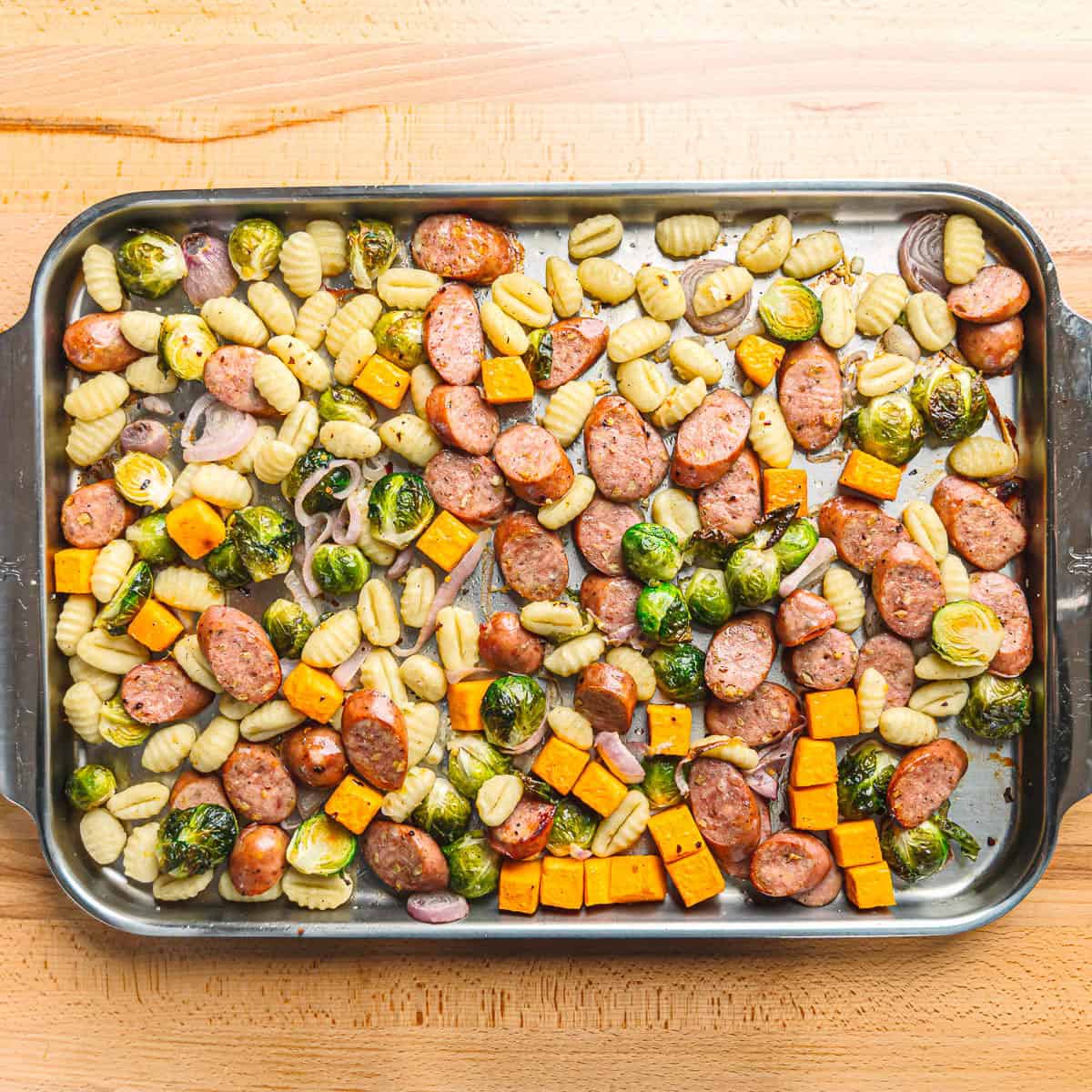 Extra large stainless steel sheet pan with sausage and veggies roasting in a hot oven.