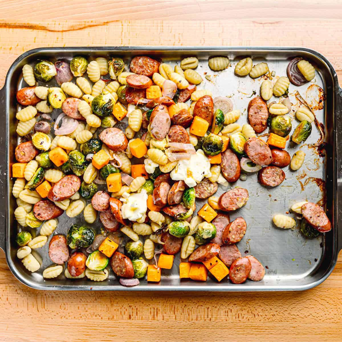Warm sheet pan of roasted chicken sausage, Brussels sprouts, squash, and gnocchi with lemon juice, mustard, honey, and butter added on top.