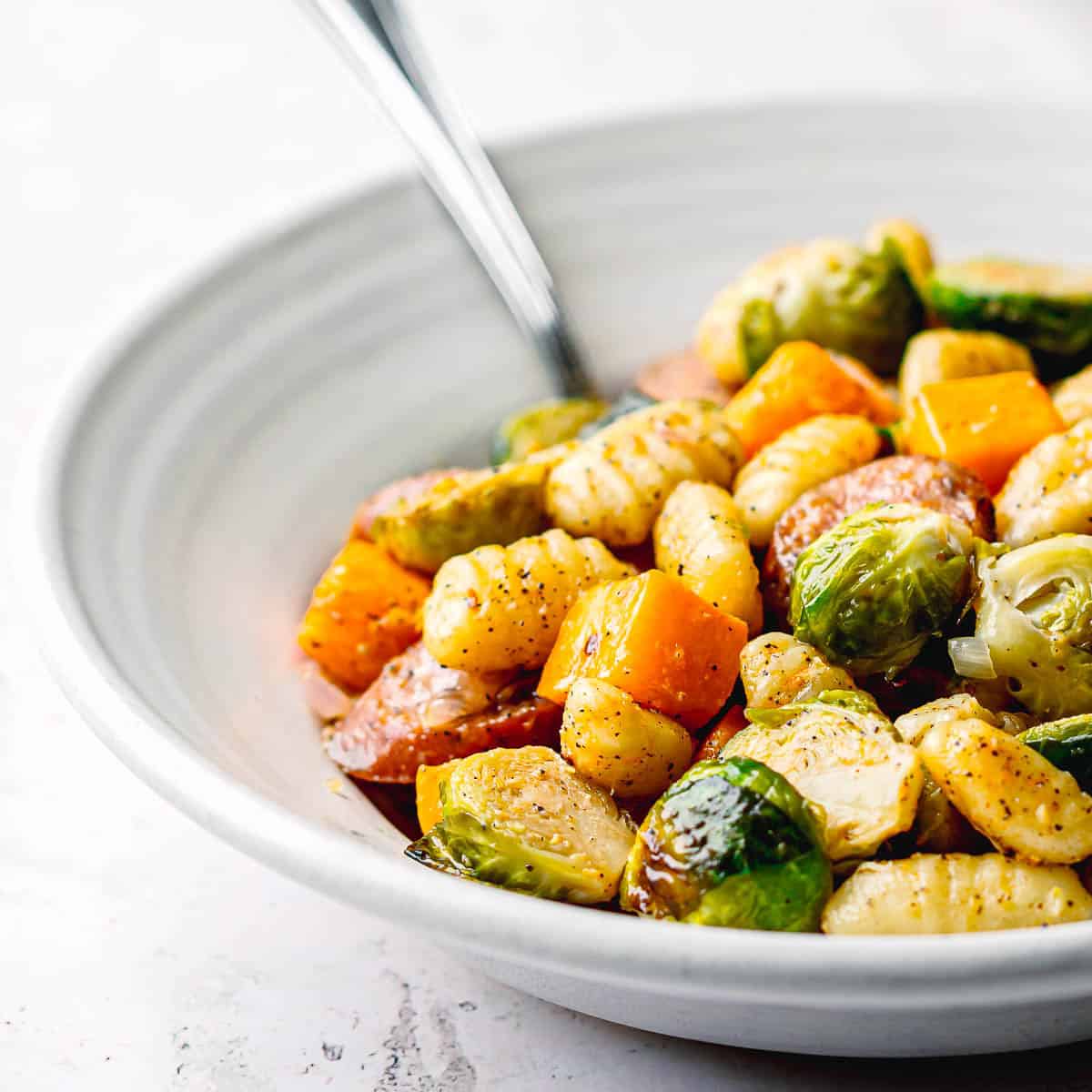 Close-up of sheet pan chicken sausage with fall vegetables in a bowl, ready to eat.