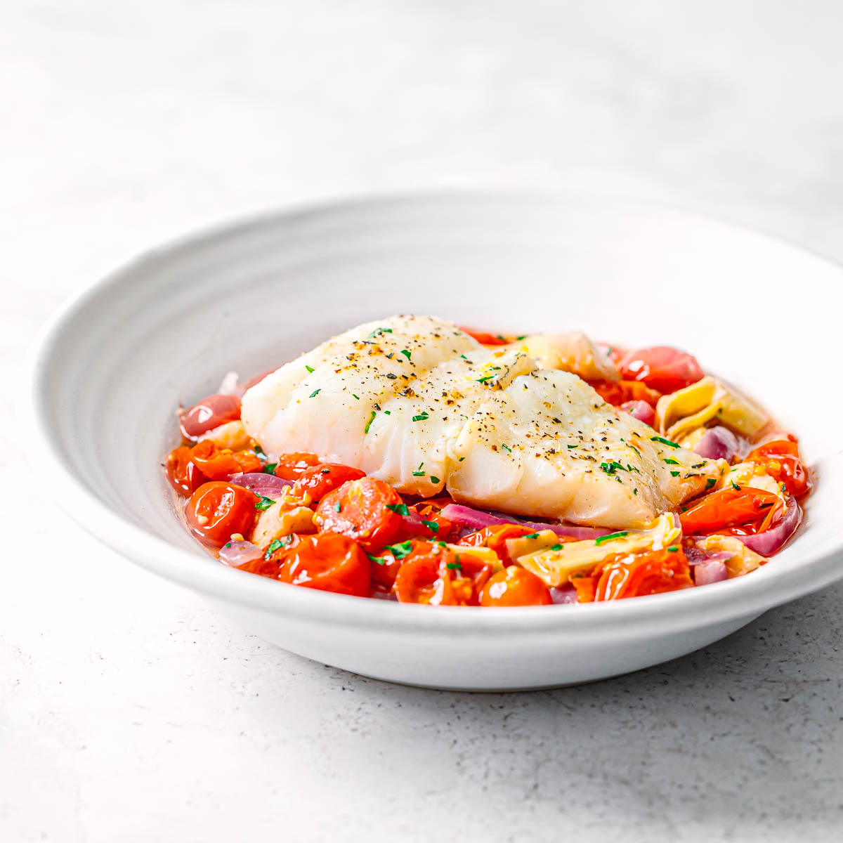 Baked Mediterranean cod with vegetables in a white bowl.