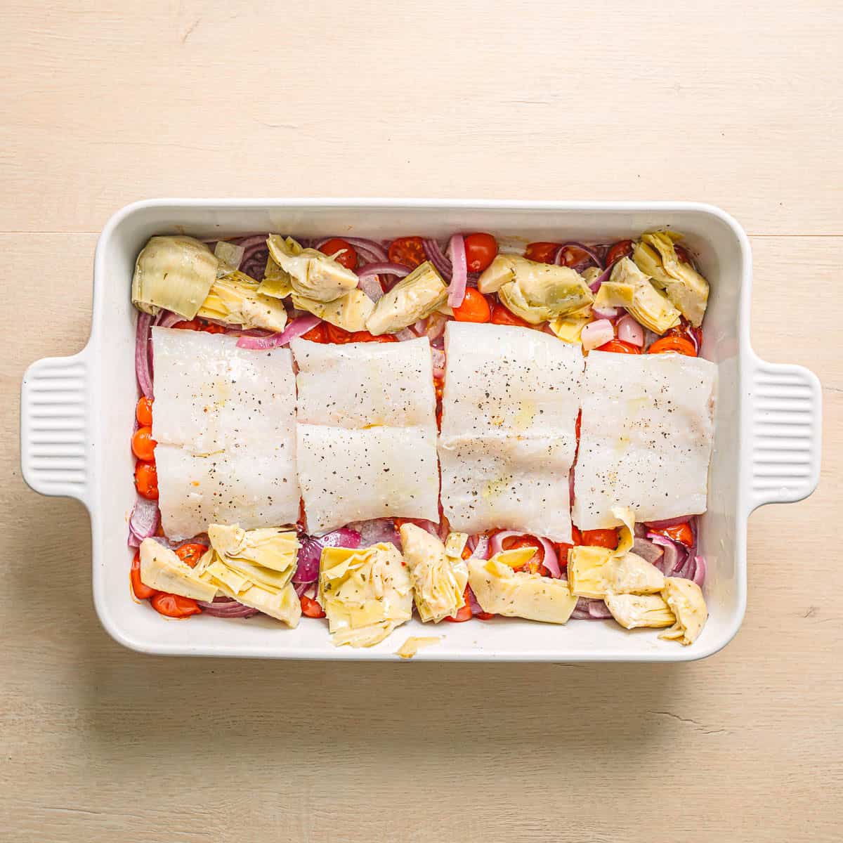 Raw cod fillets with tomatoes, artichokes, red onion, garlic, lemon, olive oil, and herbs.