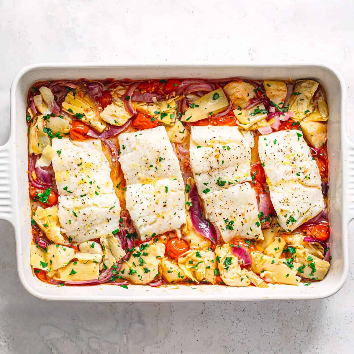 Mediterranean baked cod finished in a baking dish with roasted tomatoes, artichokes, red onion, and herbs.