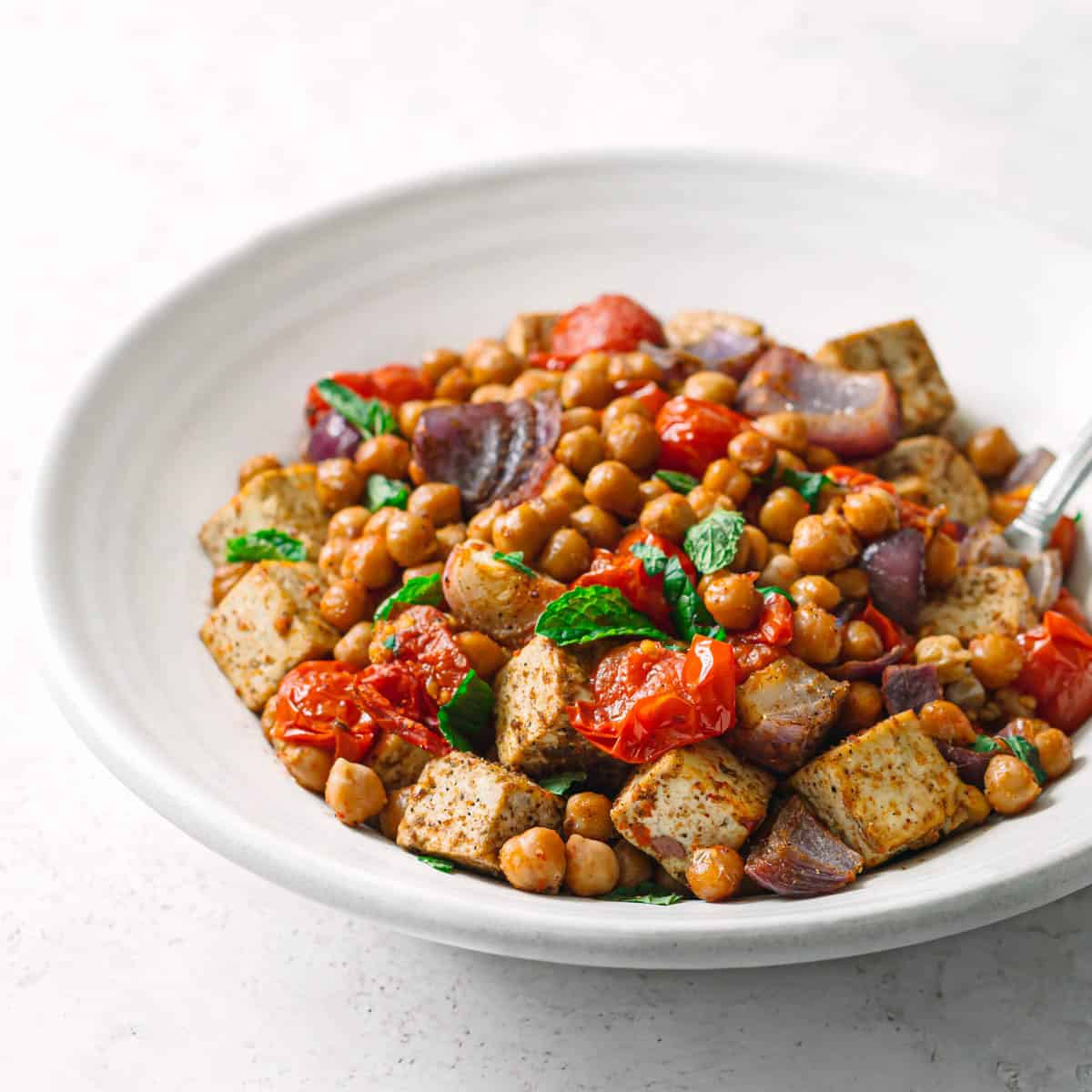 Side view of oven baked masala chickpeas with tofu and tomatoes in a white bowl.