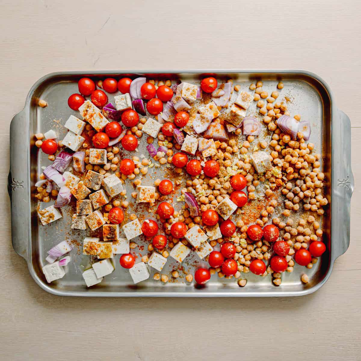 Masala chickpeas tofu and tomatoes mixed with Indian spices on a sheet pan before baking.