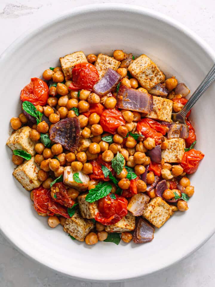Top view of oven baked masala chickpeas with tofu and blistered tomatoes in a white bowl