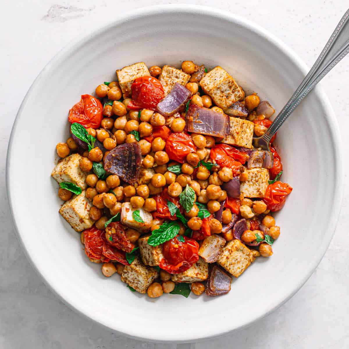 Top view of oven baked masala chickpeas with tofu and blistered tomatoes in a white bowl