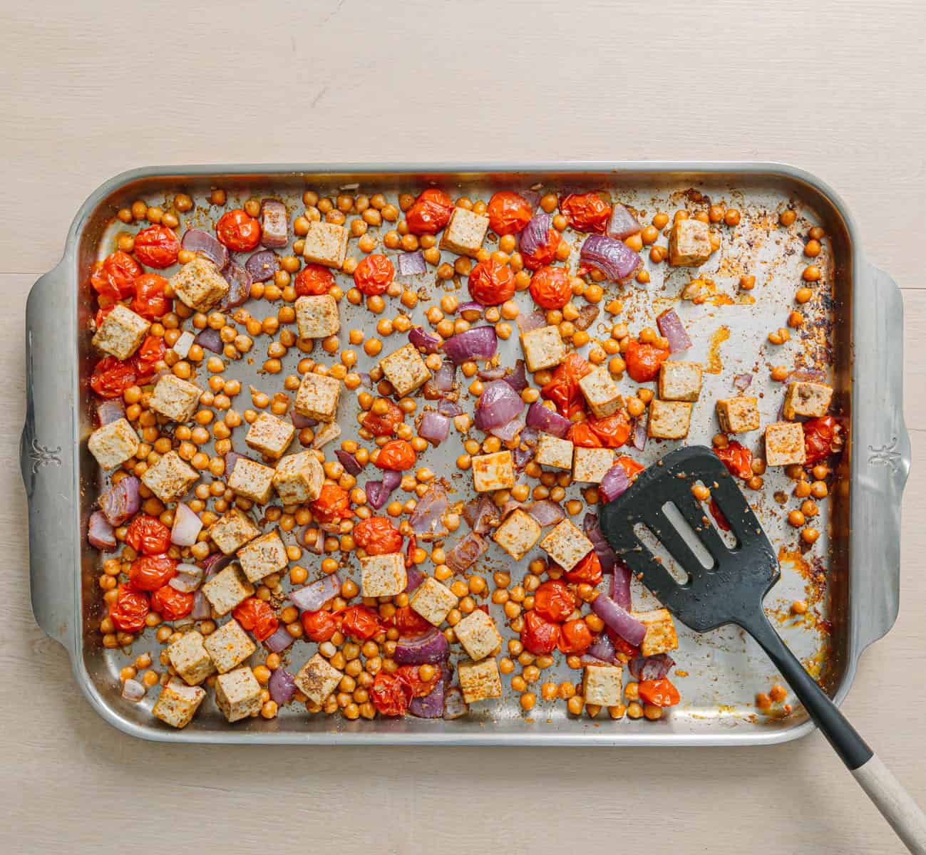 Oven baked masala chickpeas with tofu and blistered tomatoes on a sheet pan.