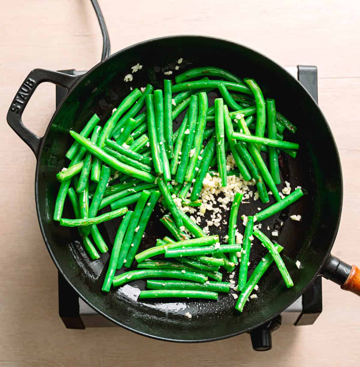 Fresh green beans sautéing in a pan with olive oil and garlic.