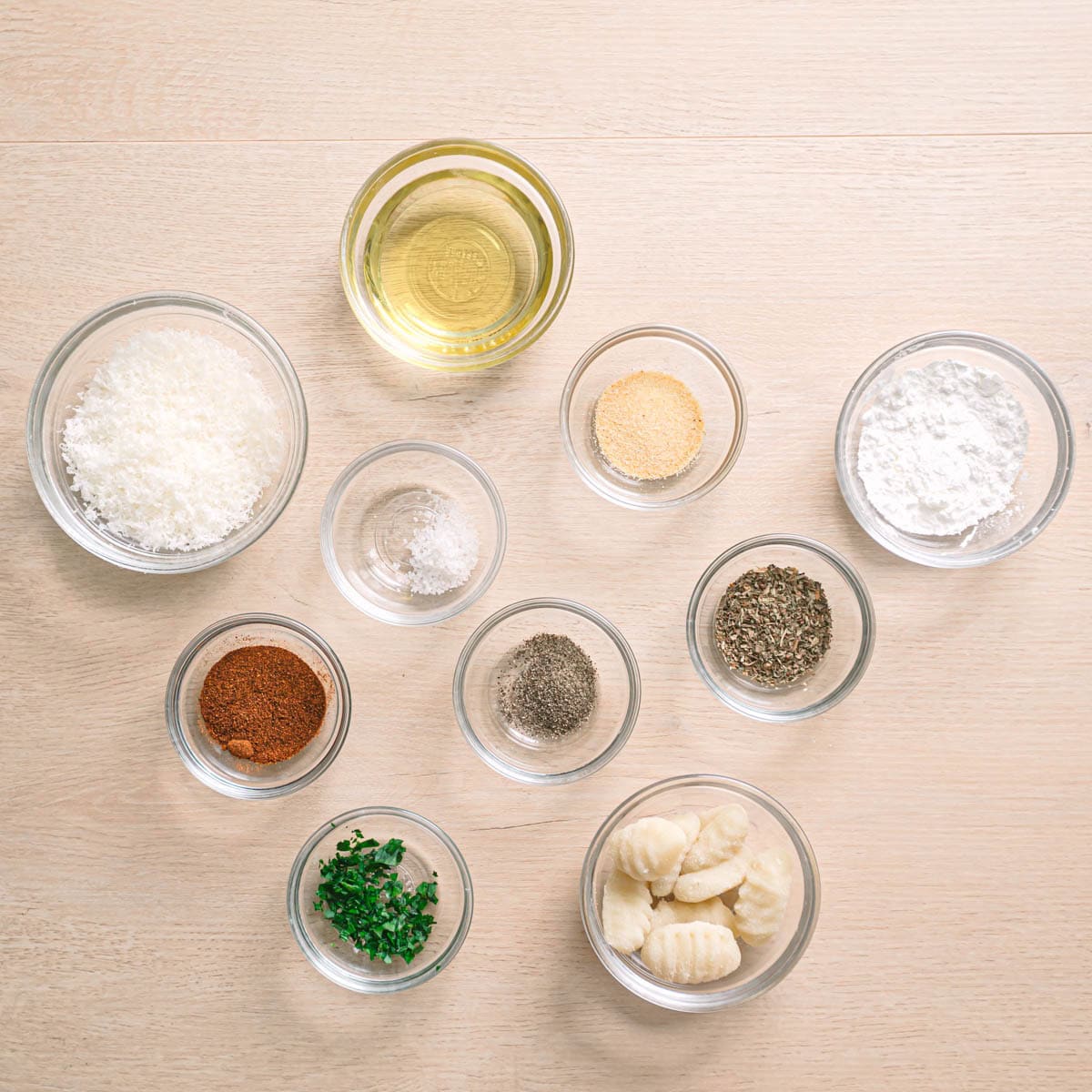 Air fryer gnocchi ingredients on a table including gnocchi, parmesan, dried basil, oil, garlic, and paprika.