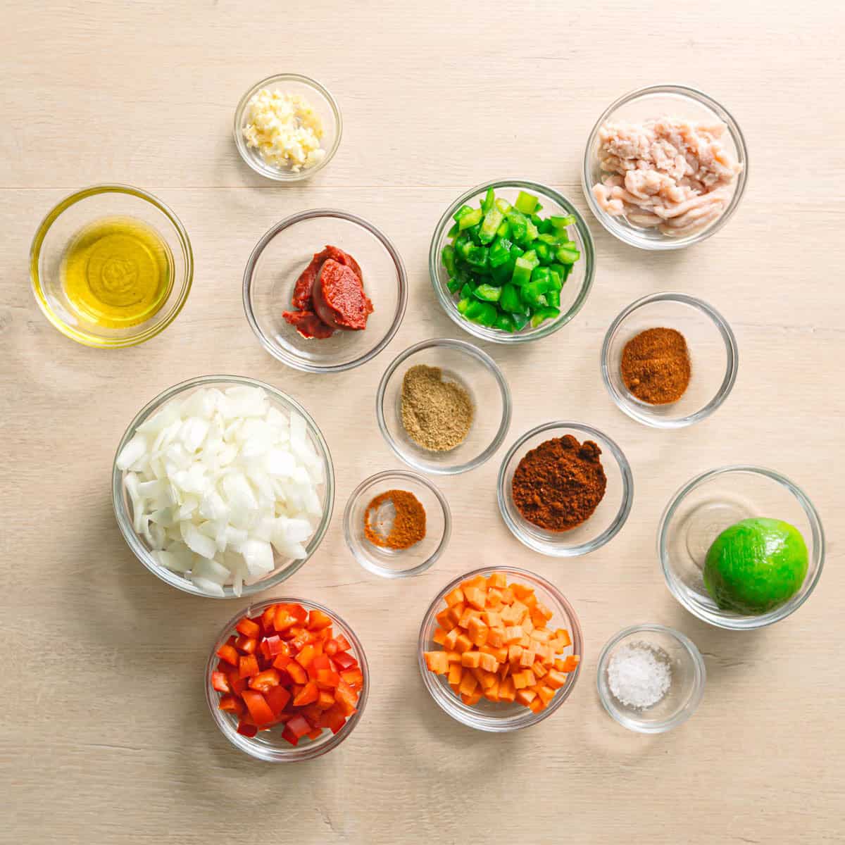 Fresh ingredients for Easy Ground Chicken Stir-Fry on a table, including ground chicken, bell peppers, onion, carrot, garlic, lime, and spices.