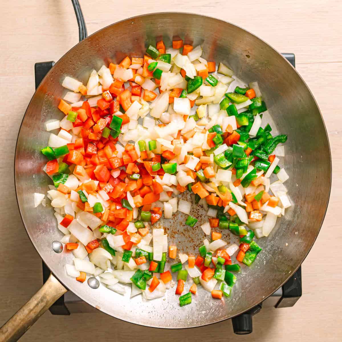 Bell peppers , chopped onion, and garlic cooking in a pan with vegetables for easy ground chicken stir fry.