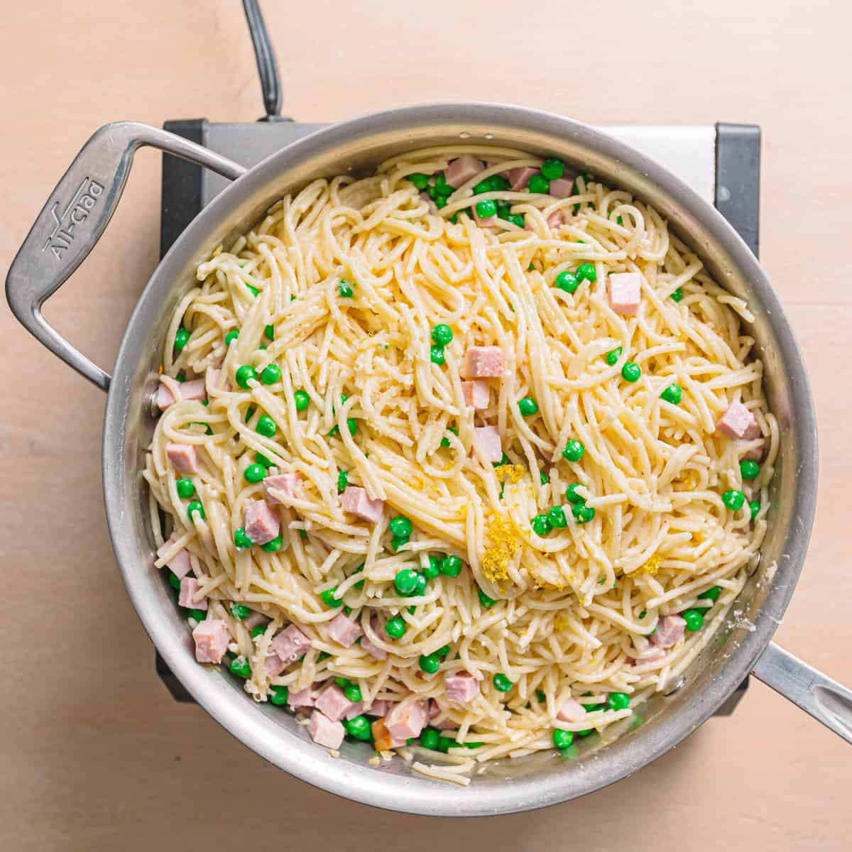 Lemon zest and fresh lemon juice being added to creamy pasta in a skillet.