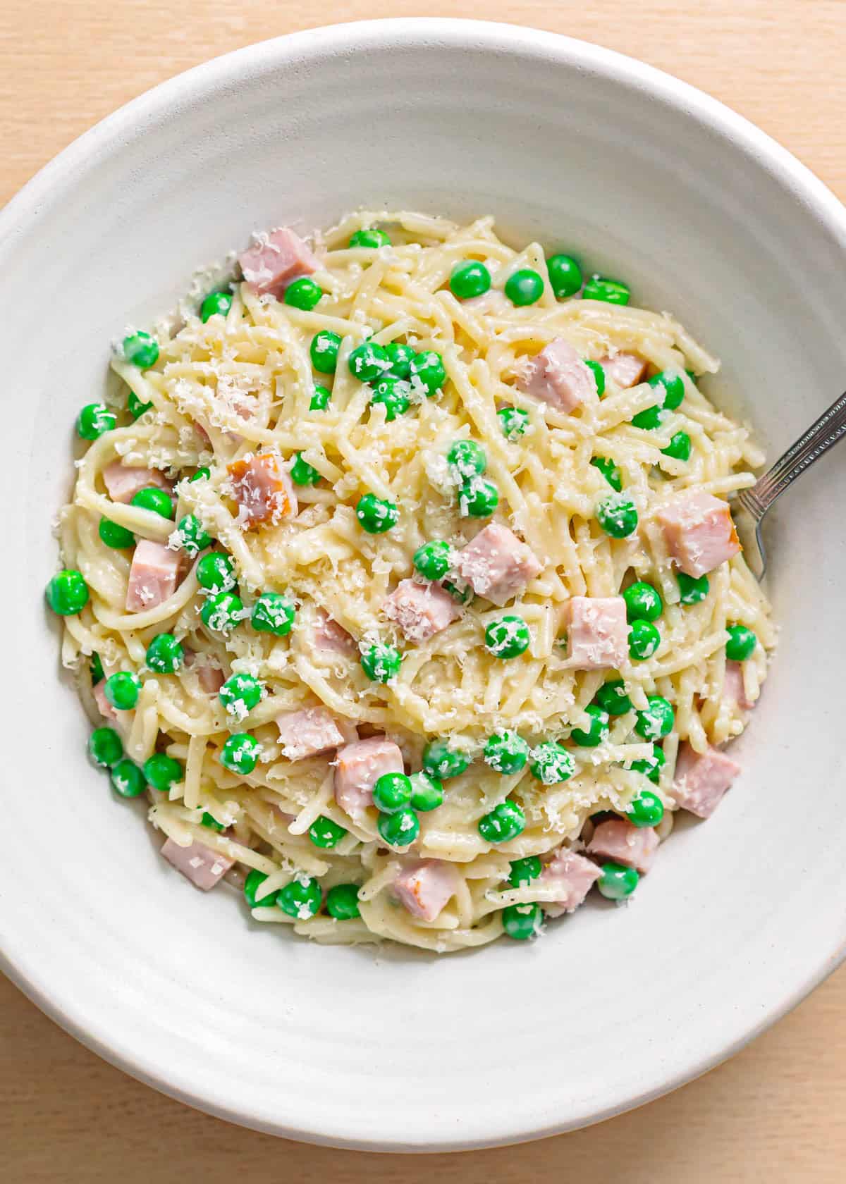 Top view of pasta with ham and peas in a serving bowl.