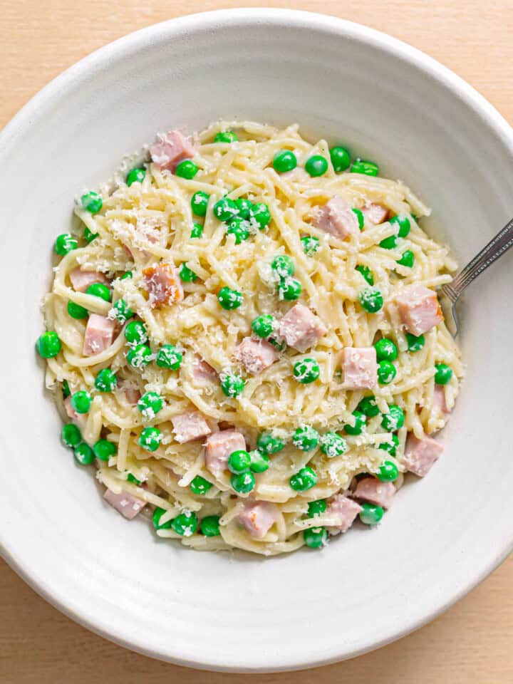 Creamy pasta with ham and peas served in a white ceramic bowl.