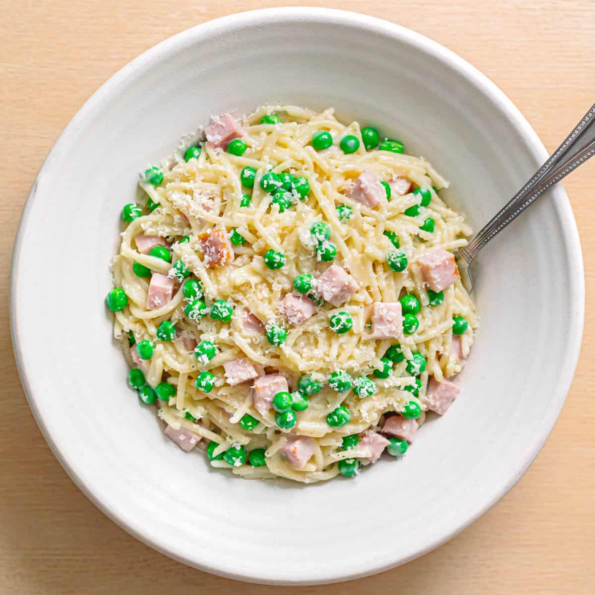 Creamy pasta with ham and peas served in a white ceramic bowl.