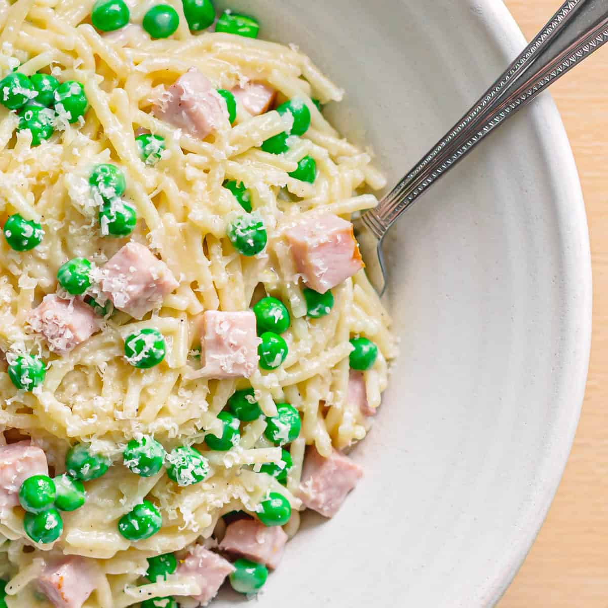 Homemade pasta with ham and peas plated in a ceramic dish.