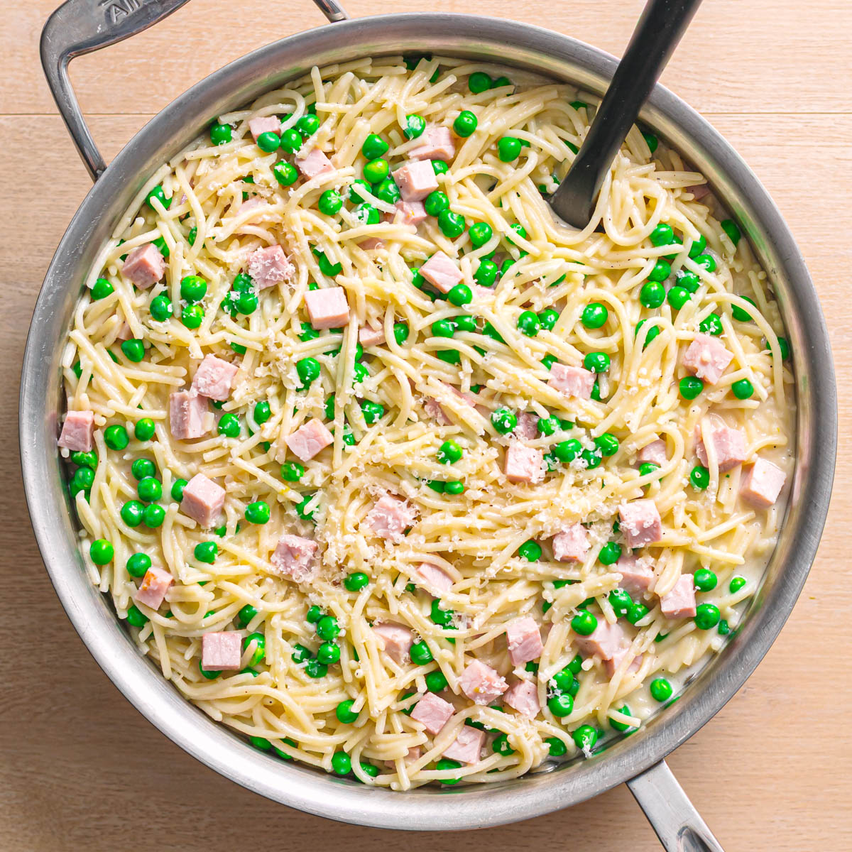 Creamy pasta with ham and peas served in a skillet topped with parmesan cheese.